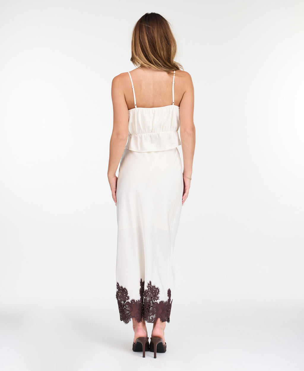 A woman modeling a white midi with dark brown lace detailing on the bodice of tank and hem, standing against a plain white studio background.