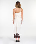 A woman modeling a white midi with dark brown lace detailing on the bodice of tank and hem, standing against a plain white studio background.