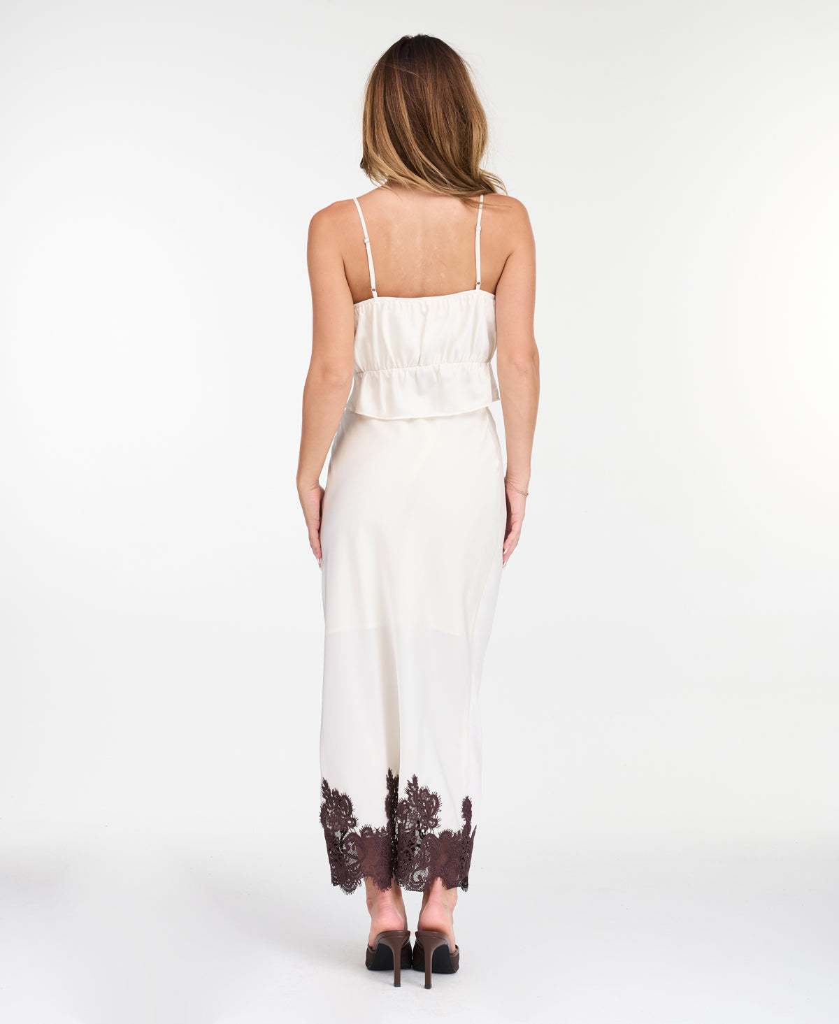 A woman modeling a white midi with dark brown lace detailing on the bodice of tank and hem, standing against a plain white studio background.