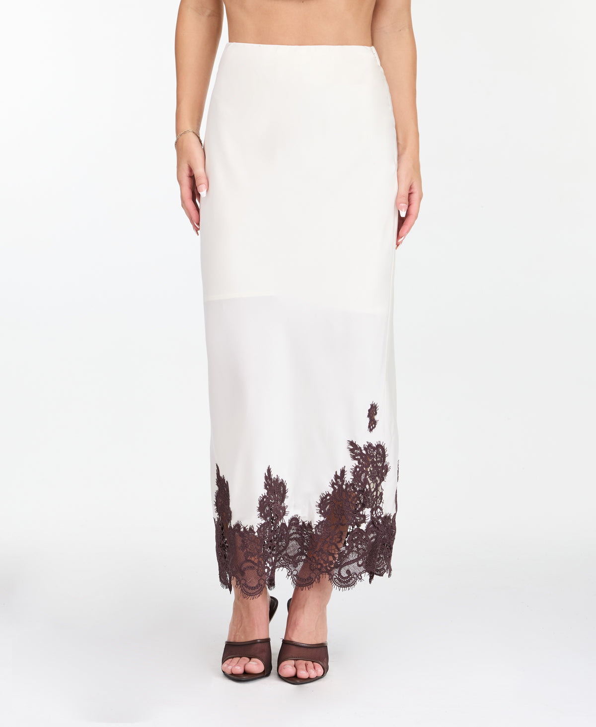 A woman modeling a white midi with dark brown lace detailing on the bodice of tank and hem, standing against a plain white studio background.