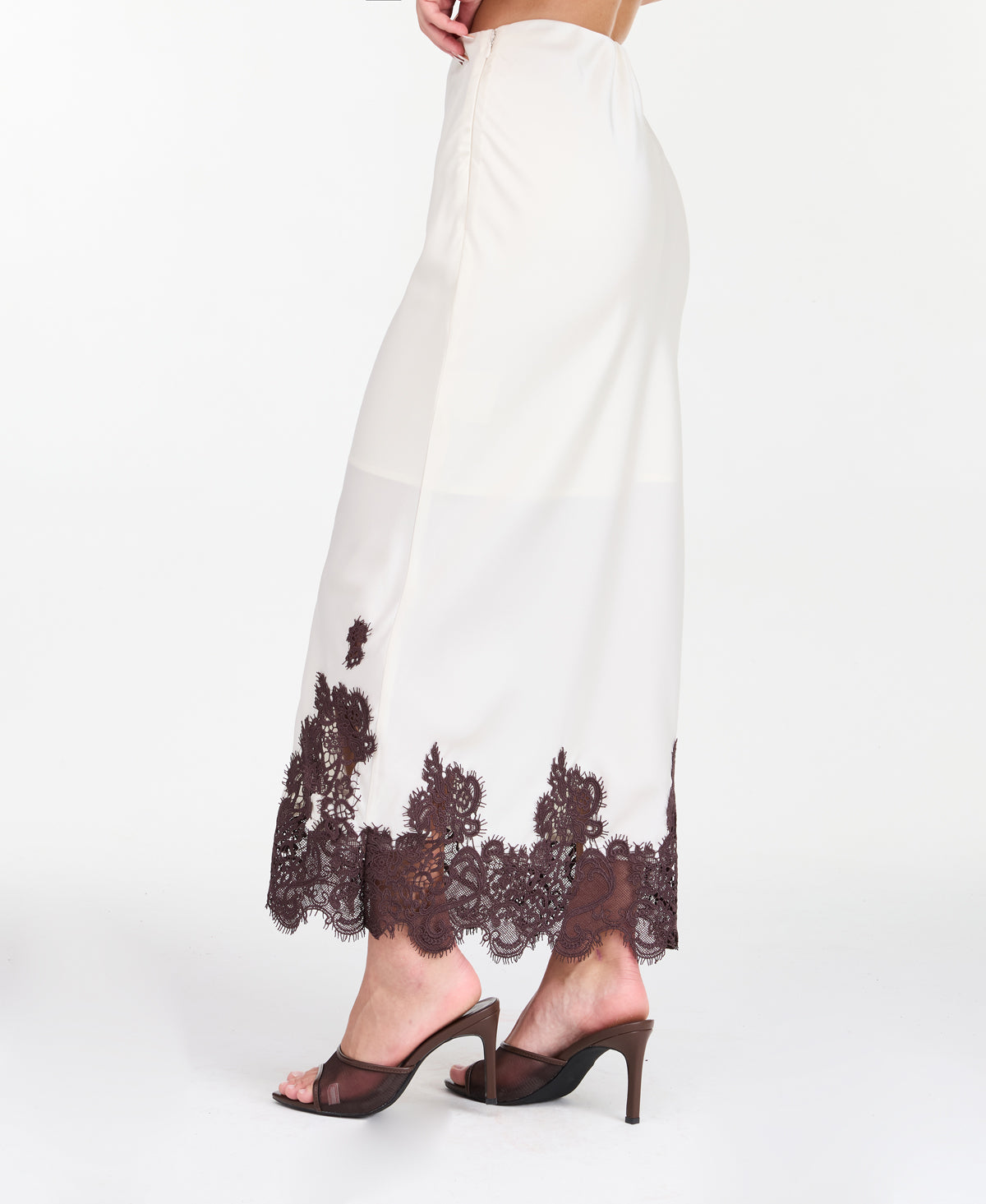 A woman modeling a white midi with dark brown lace detailing on the bodice of tank and hem, standing against a plain white studio background.