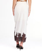 A woman modeling a white midi with dark brown lace detailing on the bodice of tank and hem, standing against a plain white studio background.