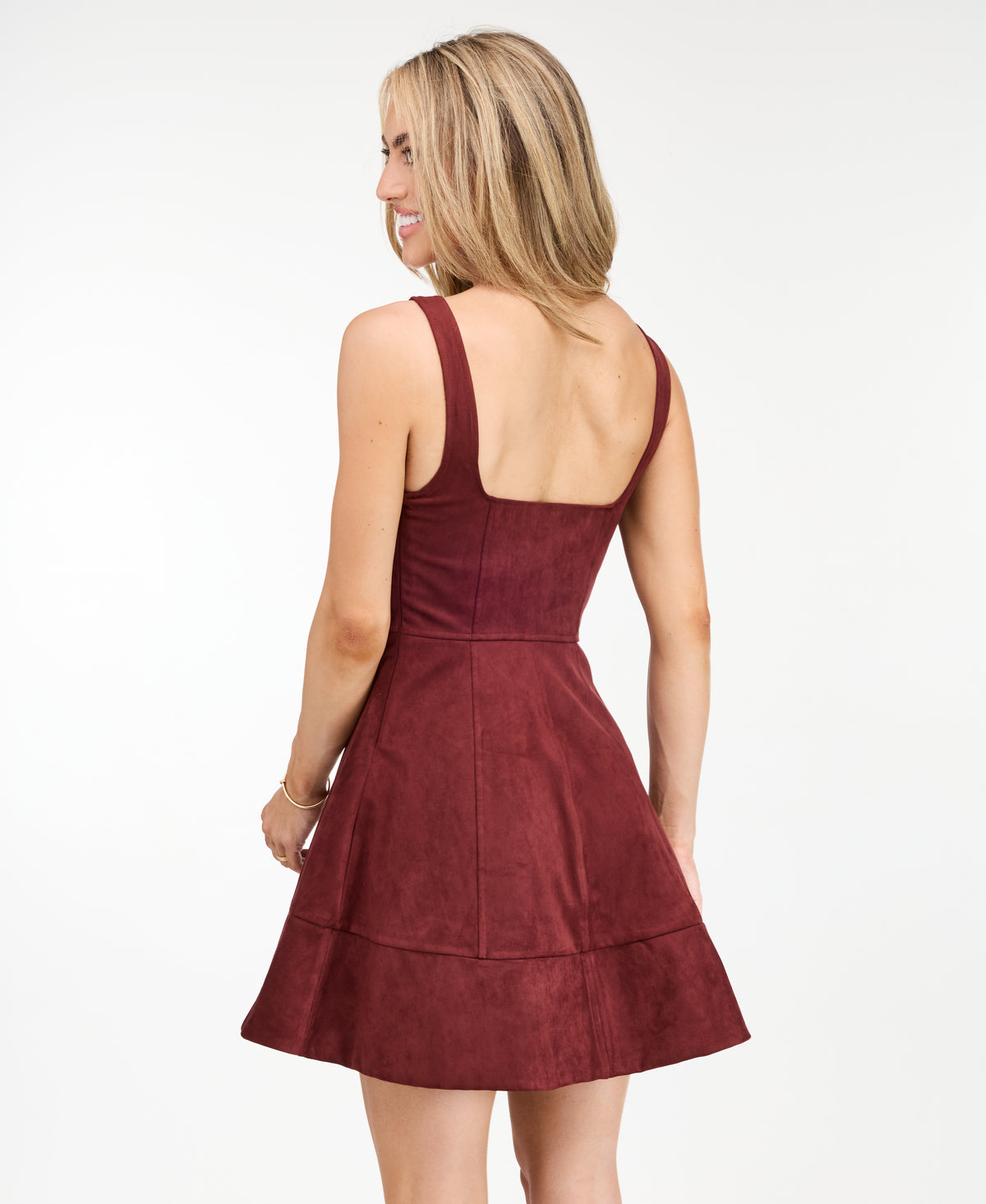 A woman modeling a sleeveless, fit and flared mini dress in a deep burgundy color, paired with tan high-heeled sandals, photographed against a seamless white studio background.