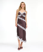A woman modeling a dark brown and white polka dot slip dress with white lace trim, photographed against a solid white studio background.