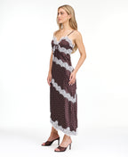 A woman modeling a dark brown and white polka dot slip dress with white lace trim, photographed against a solid white studio background.
