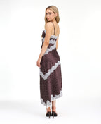 A woman modeling a dark brown and white polka dot slip dress with white lace trim, photographed against a solid white studio background.