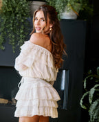 Jessie wearing an ivory off shoulder dress with lace and ruffle details throughout. 
