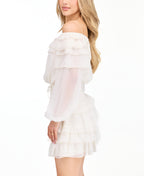 A model wearing an ivory off shoulder dress with shear bubble sleeves. The dress consists of a  smocked waistband and ruffle lace details throughout the neckline and skirt 