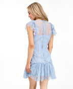 A woman modeling a light blue lace mini dress with ruffled cap sleeves and brown knee-high boots, photographed against a plain white studio background.