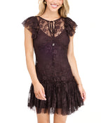 A woman modeling a dark brown lace mini dress with ruffled cap sleeves and tie detail at the neckline, paired with dark brown knee-high boots, against a plain white studio background.