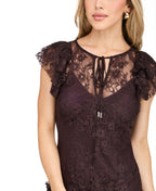 A woman modeling a dark brown lace mini dress with ruffled cap sleeves and tie detail at the neckline, paired with dark brown knee-high boots, against a plain white studio background.