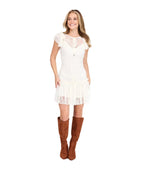 A woman modeling a short white lace dress with ruffled cap sleeves and brown knee-high suede boots, standing against a plain white studio background.