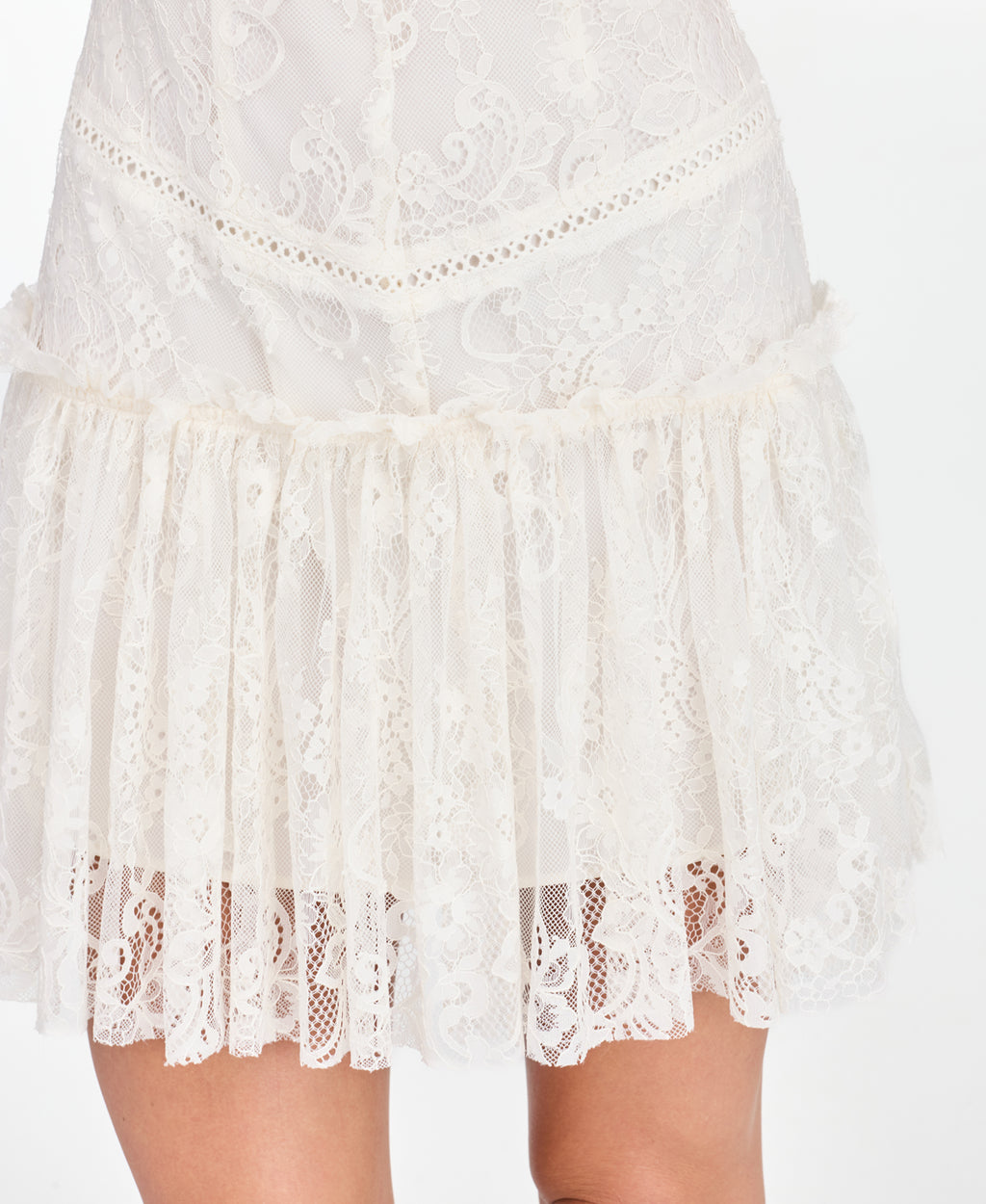 A woman modeling a short white lace dress with ruffled cap sleeves and brown knee-high suede boots, standing against a plain white studio background.