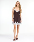 A woman modeling a short brown ribbed mini dress with white lace trim along the neckline and hem, paired with dark brown heeled sandals, against a plain white studio background.