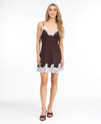A woman modeling a short brown ribbed mini dress with white lace trim along the neckline and hem, paired with dark brown heeled sandals, against a plain white studio background.