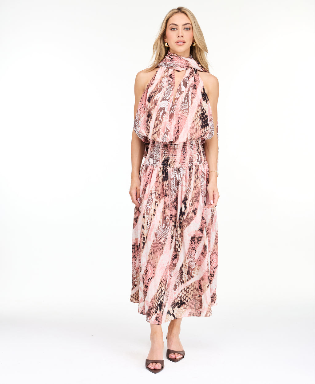 Model wearing a pink snake print midi dress with a smocked waistband and neck scarf standing against a white backdrop