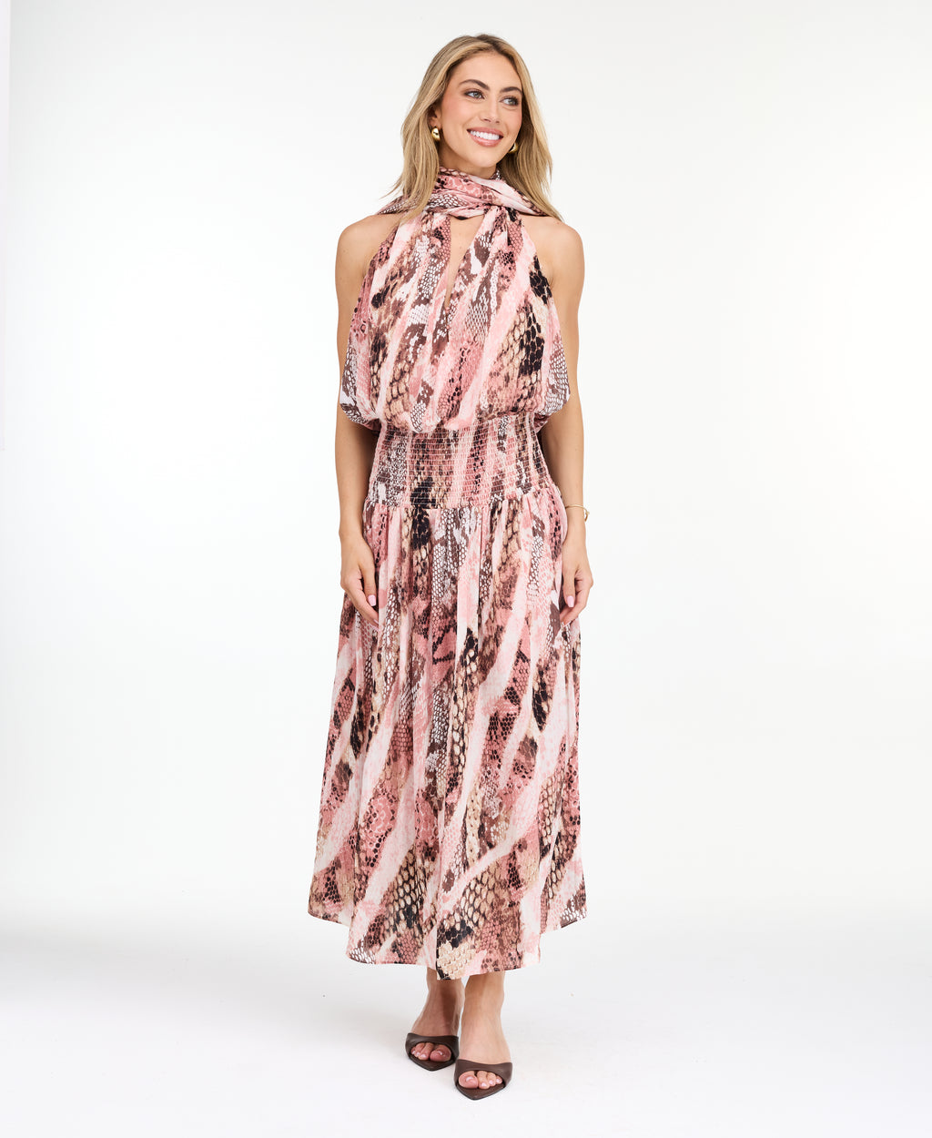 Model wearing a pink snake print midi dress with a smocked waistband and neck scarf standing against a white backdrop