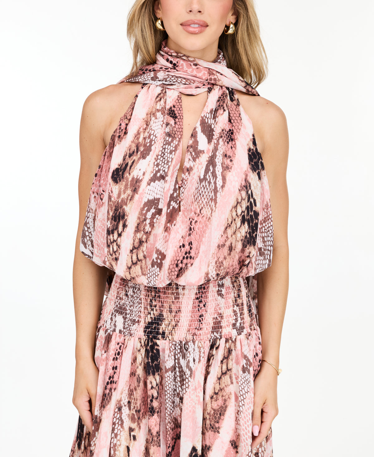 Model wearing a pink snake print midi dress with a smocked waistband and neck scarf standing against a white backdrop