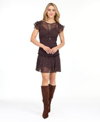 A woman modeling a short brown chiffon dress with a white polka dot pattern, ruffled cap sleeves, and a tie neckline, paired with brown knee-high boots against a plain white background.