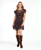 A woman modeling a short brown chiffon dress with a white polka dot pattern, ruffled cap sleeves, and a tie neckline, paired with brown knee-high boots against a plain white background.