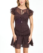 A woman modeling a short brown chiffon dress with a white polka dot pattern, ruffled cap sleeves, and a tie neckline, paired with brown knee-high boots against a plain white background.