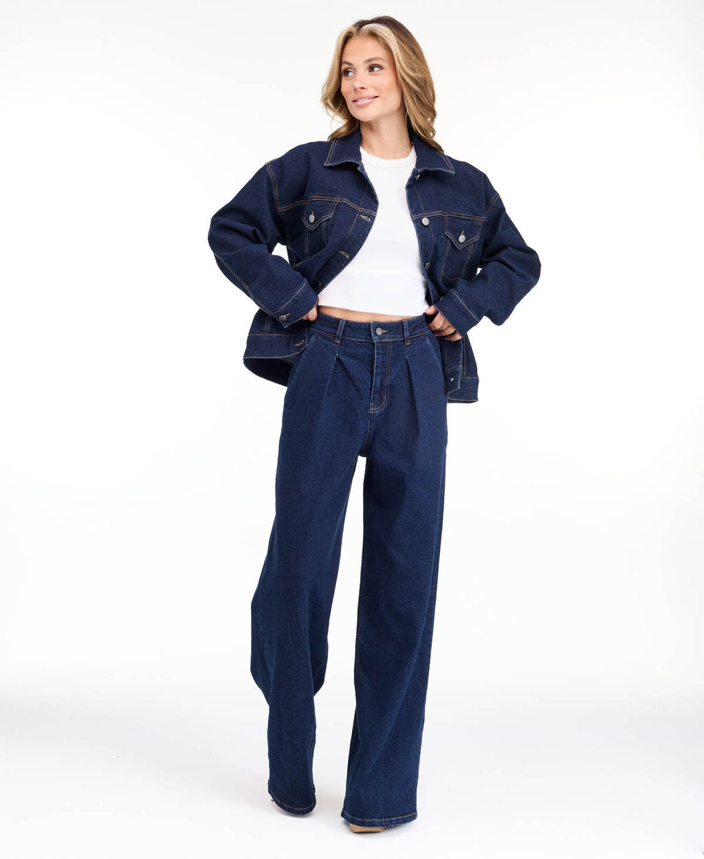 A model wearing dark blue wide-leg denim jeans with a high waist and front pleats, shown from the waist down on a white studio background.