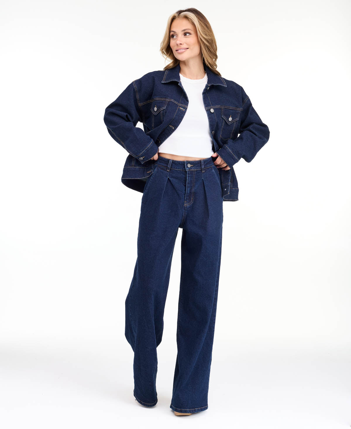 A model wearing dark blue wide-leg denim jeans with a high waist and front pleats, shown from the waist down on a white studio background.