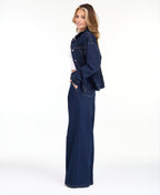 A woman modeling a dark denim wash jacket and matching wide-leg jeans over a white top, photographed against a seamless white studio background.