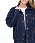 A woman modeling a dark denim wash jacket and matching wide-leg jeans over a white top, photographed against a seamless white studio background.