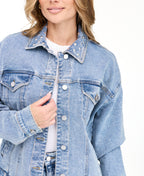 A woman modeling a light blue denim jacket with studs on the neckline and matching wide-leg jeans against a plain white studio background.