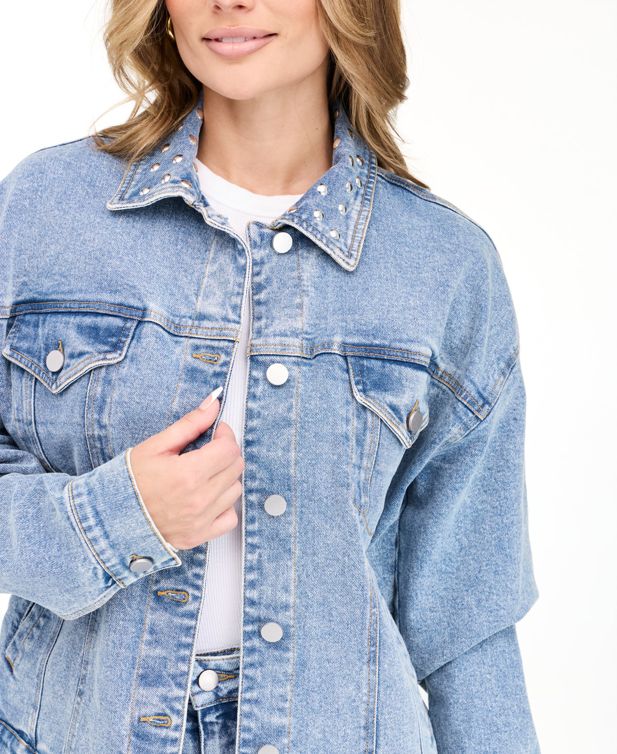 A woman modeling a light blue denim jacket with studs on the neckline and matching wide-leg jeans against a plain white studio background.