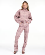 A woman wearing a dusty rose snakeskin print zip-up jacket with a mock neck, paired with pants, against a plain white background.