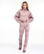 A woman modeling a dusty rose pink and brown snakeskin pattern, featuring a cropped zip-up jacket and matching pants, set against a plain white studio background.