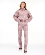 A woman modeling a dusty rose pink and brown snakeskin pattern, featuring a cropped zip-up jacket and matching pants, set against a plain white studio background.