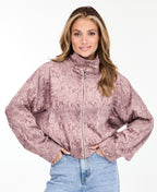A woman wearing a dusty rose snakeskin print zip-up jacket with a mock neck, paired with pants, against a plain white background.