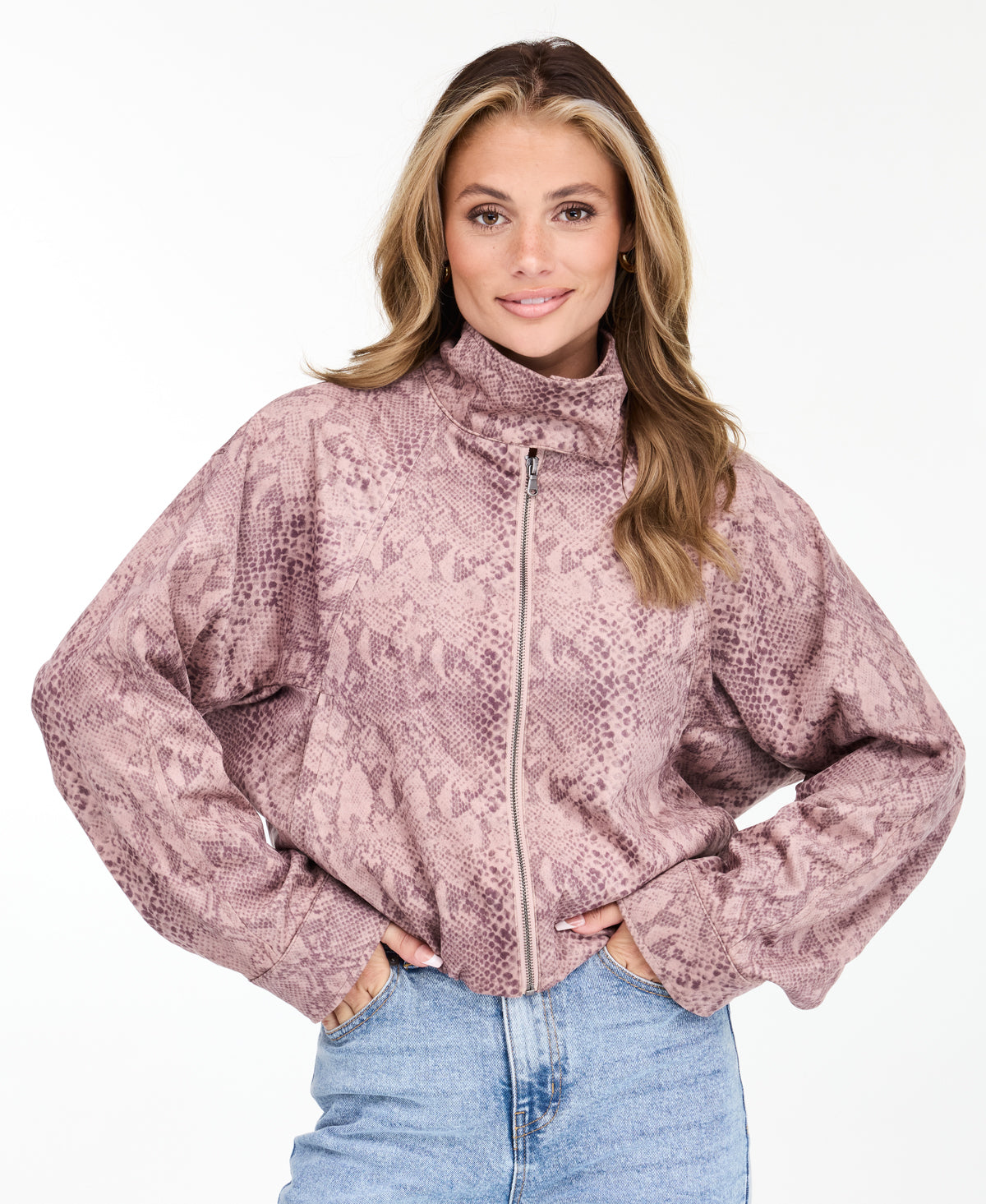A woman wearing a dusty rose snakeskin print zip-up jacket with a mock neck, paired with pants, against a plain white background.