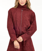 A woman modeling a matching burgundy zip-up jacket, fit and flare dress,  and tall knee-high boots against a plain white studio background.