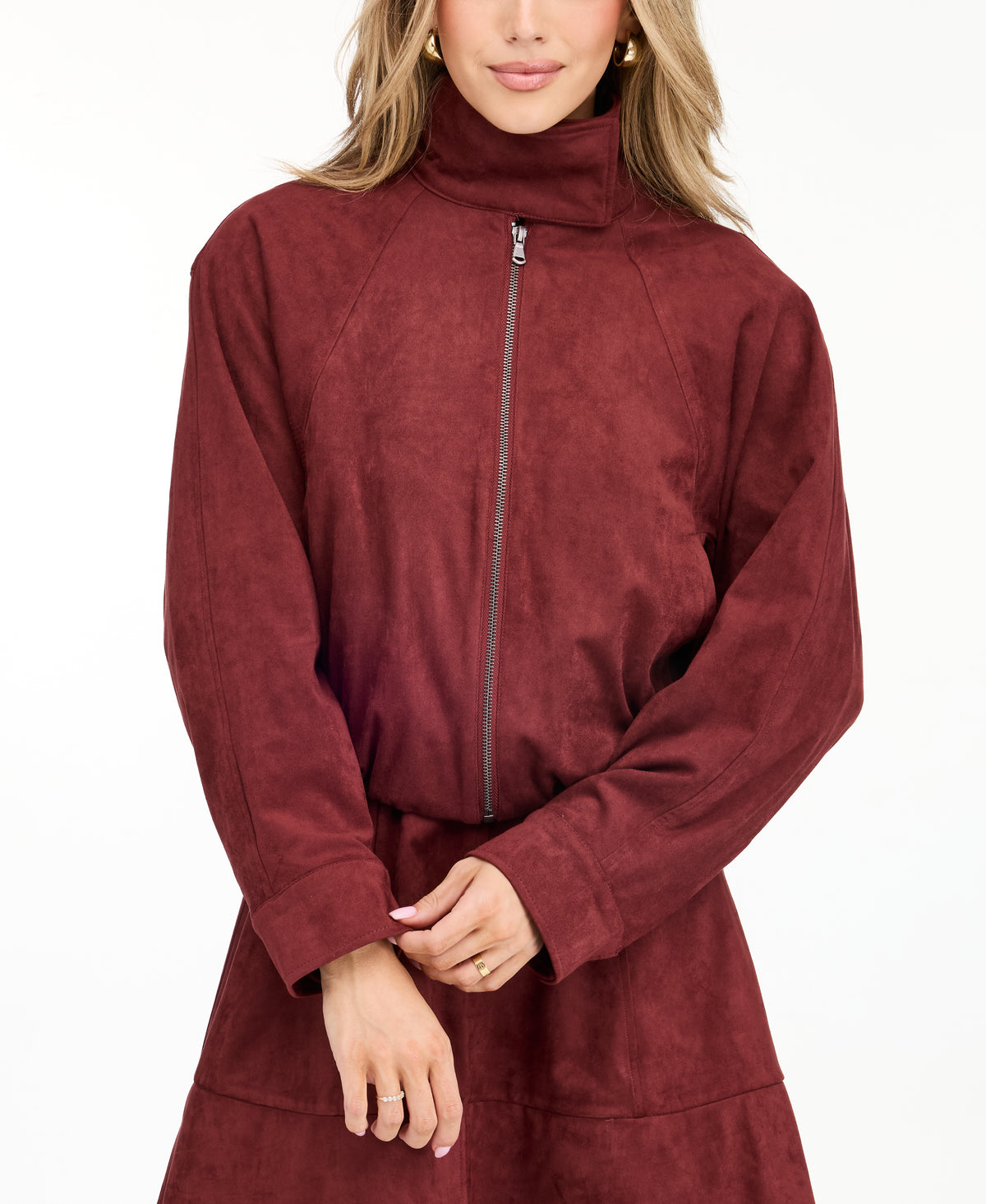 A woman modeling a matching burgundy zip-up jacket, fit and flare dress,  and tall knee-high boots against a plain white studio background.