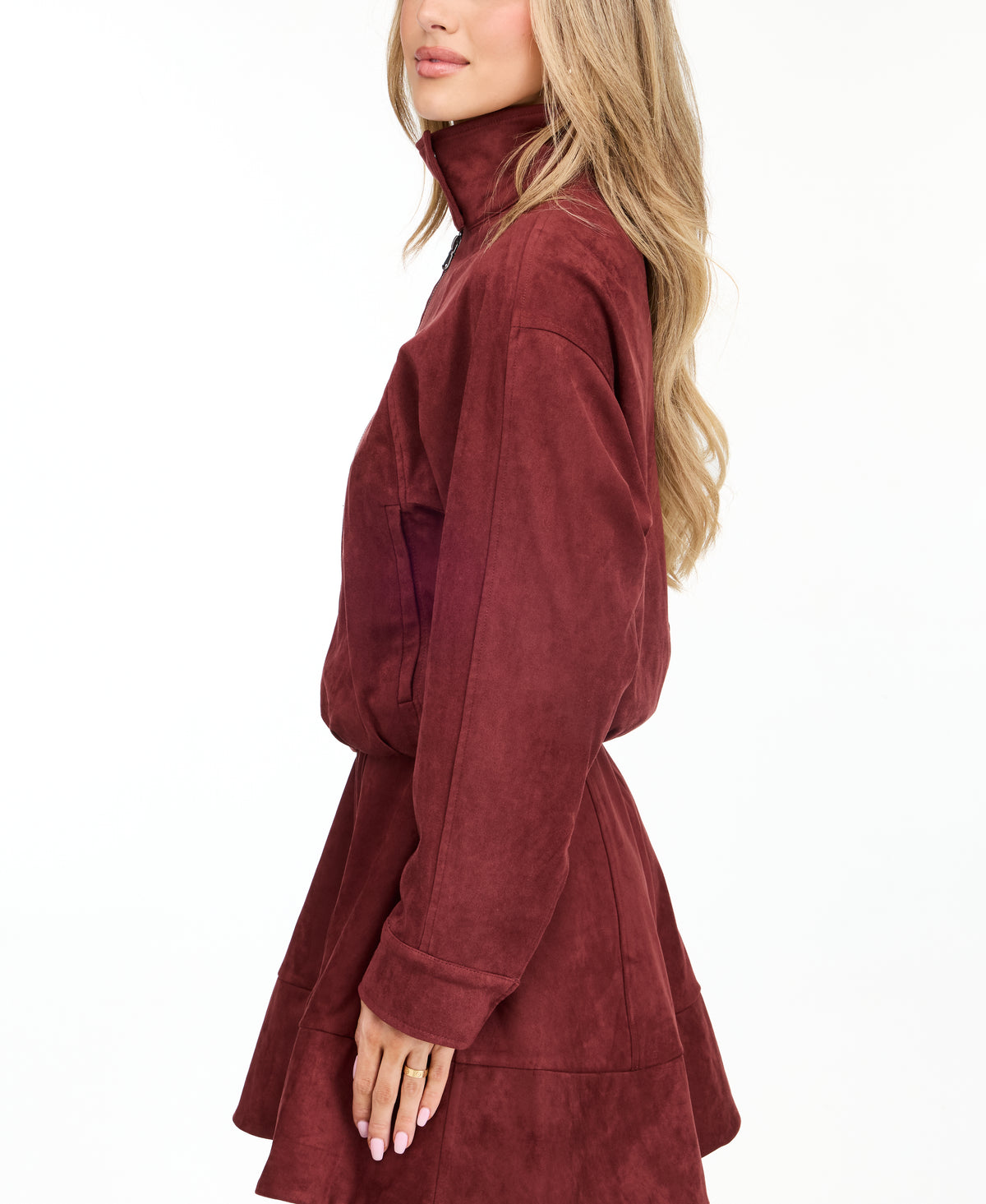 A woman modeling a matching burgundy zip-up jacket, fit and flare dress,  and tall knee-high boots against a plain white studio background.