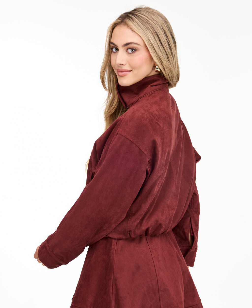 A woman modeling a matching burgundy zip-up jacket, fit and flare dress,  and tall knee-high boots against a plain white studio background.