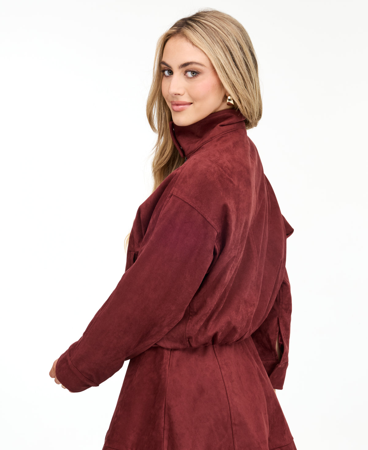 A woman modeling a matching burgundy zip-up jacket, fit and flare dress,  and tall knee-high boots against a plain white studio background.