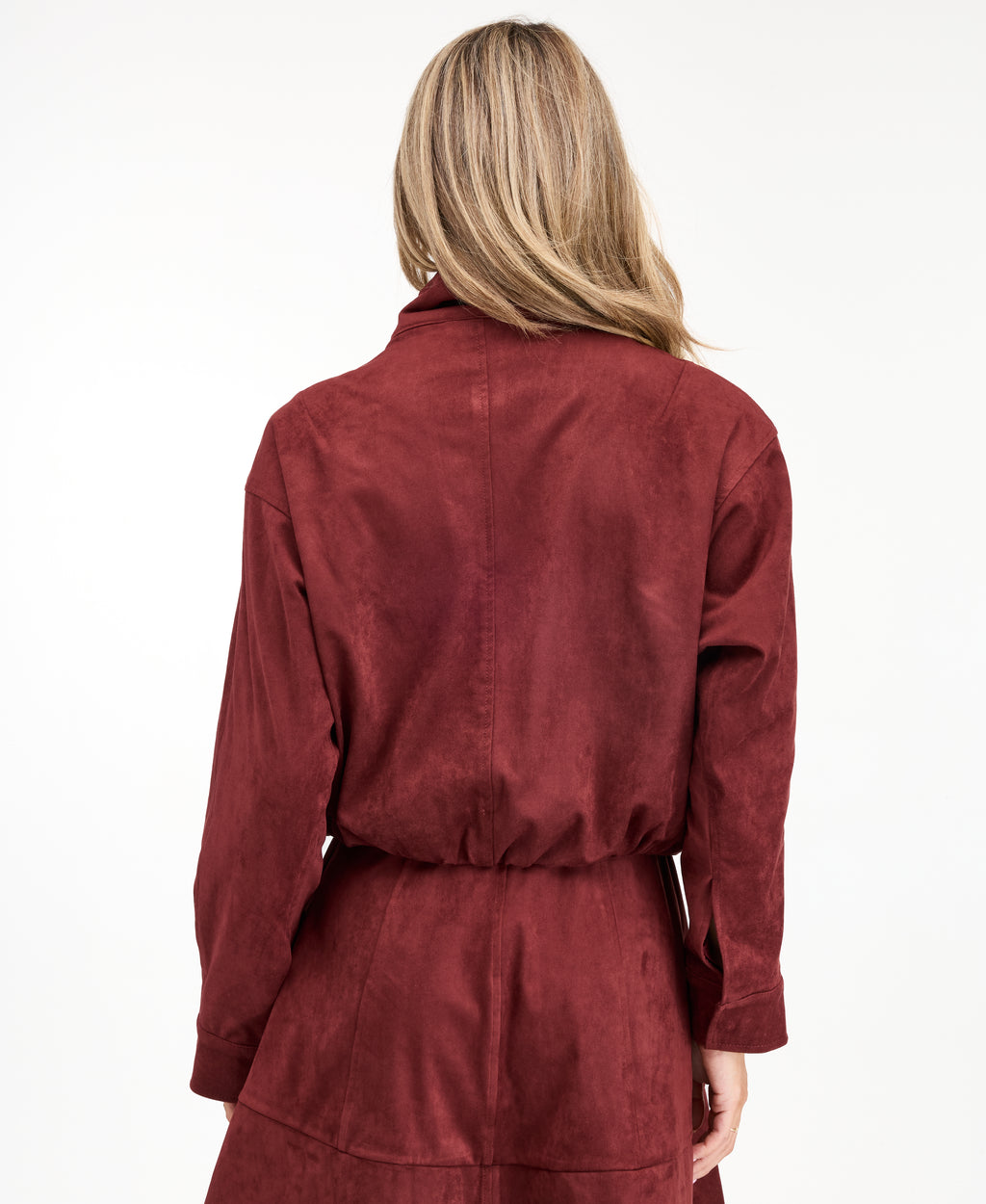 A woman modeling a matching burgundy zip-up jacket, fit and flare dress,  and tall knee-high boots against a plain white studio background.
