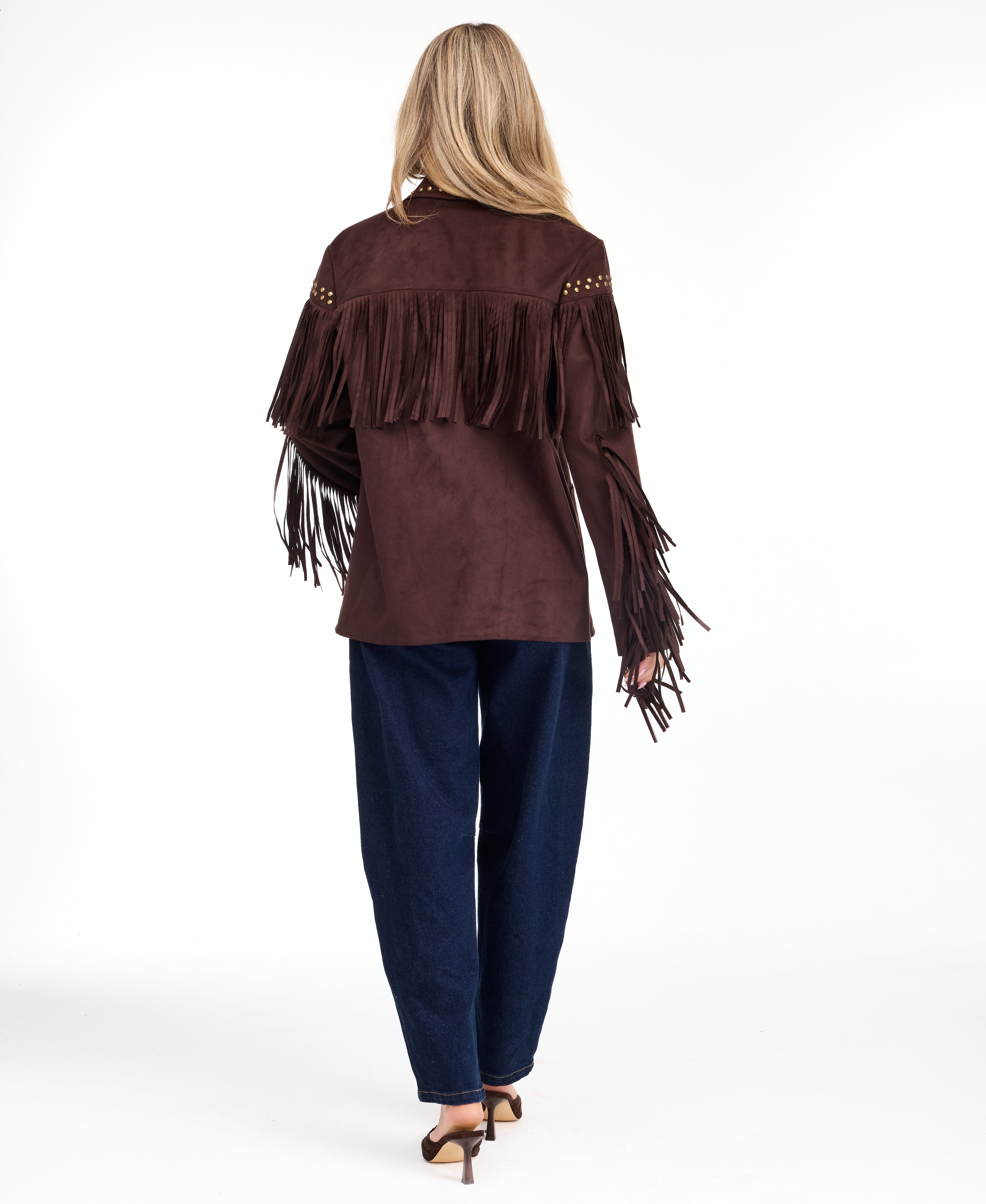 A woman modeling a dark brown suede fringe jacket with gold-tone studs and buttons, paired with brown and denim patchwork pants and brown pointed-toe heels, against a plain white studio background.