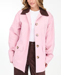 A woman modeling a light pink oversized jacket with dark brown collar and buttons, worn over a white top and paired with a brown pants, on a white studio background.