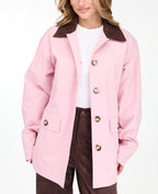 A woman modeling a light pink oversized jacket with dark brown collar and buttons, worn over a white top and paired with a brown pants, on a white studio background.