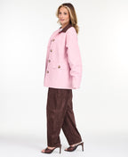 A woman modeling a light pink oversized jacket with dark brown collar and buttons, worn over a white top and paired with a brown pants, on a white studio background.