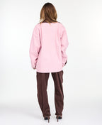 A woman modeling a light pink oversized jacket with dark brown collar and buttons, worn over a white top and paired with a brown pants, on a white studio background.
