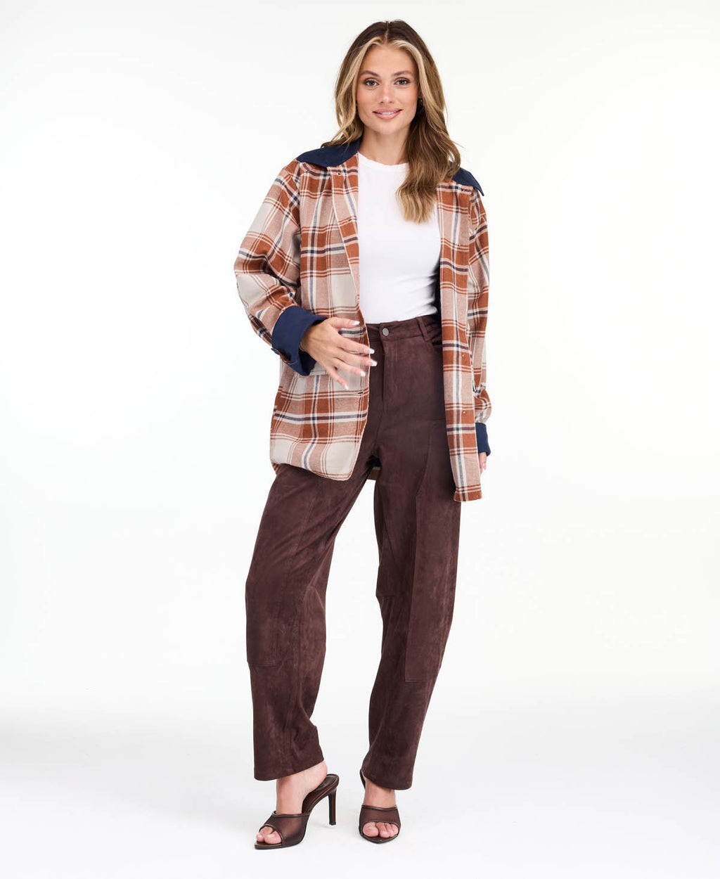 Model wearing a light brown plaid coat with navy blue contrast lapels and cuffs, styled over a white top and brown pants against a plain white background.