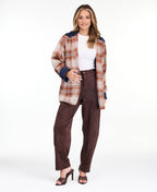 Model wearing a light brown plaid coat with navy blue contrast lapels and cuffs, styled over a white top and brown pants against a plain white background.