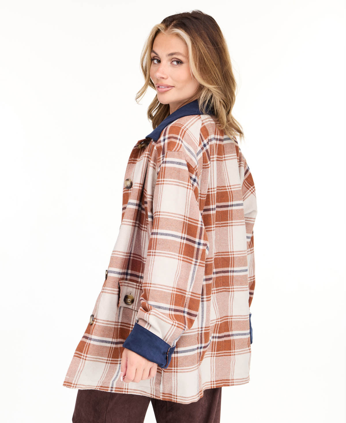 Model wearing a light brown plaid coat with navy blue contrast lapels and cuffs, styled over a white top and brown pants against a plain white background.